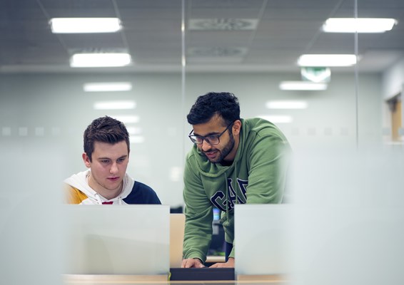 Two students studying and looking at a laptop together