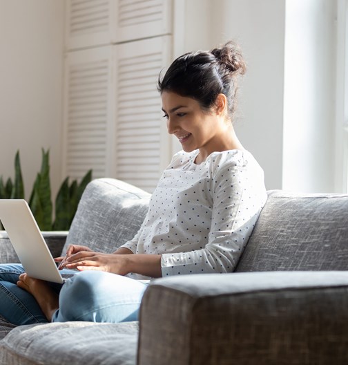 smiling women sat on the sofa working on her laptop