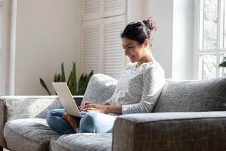 smiling women sat on the sofa working on her laptop