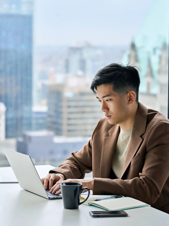 Young asian male working at a laptop with a city landscape behind him