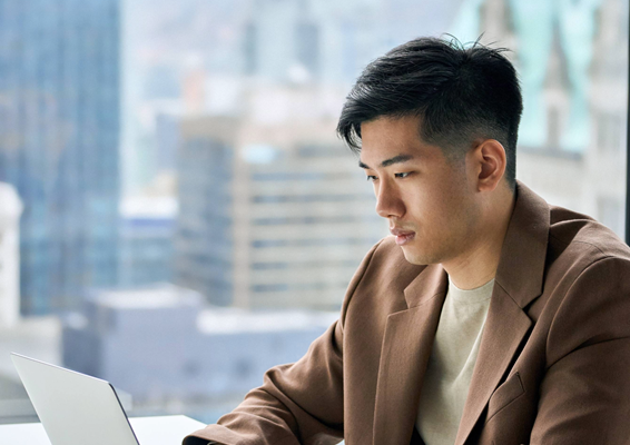 Young asian male working at a laptop with a city landscape behind him